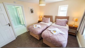 A double room with two beds, each with a headboard, bedside tables, and lamps. There is a door leading to a bathroom with a glass shower enclosure. - White Jasmine in Stroud (Stroud)