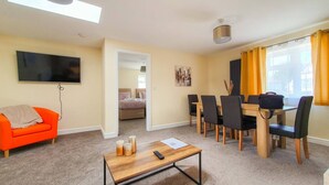 A modern living room with a bright orange sofa, a wooden coffee table, and a dining area with a table and chairs. - White Jasmine in Stroud (Stroud)