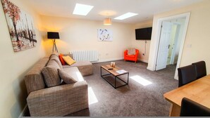 A living room with a sofa, a coffee table, a TV, and a door leading to another room. - White Jasmine in Stroud (Stroud)