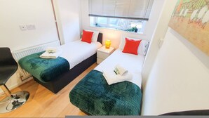 Une chambre de taille modeste, équipée de deux lits simples, d’une petite table de chevet avec une lampe, d’une chaise et d’un radiateur.