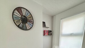 A dining area with a wooden table, grey placemats, a decorative clock, and a window with blinds.