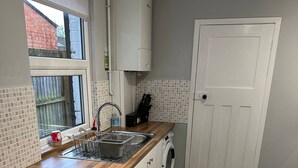 A kitchen with a wooden countertop, a built-in dishwasher, a washing machine, and a window with blinds.