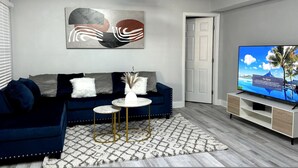 Un salon moderne avec un canapé bleu foncé, une table basse blanche et un téléviseur à écran plat posé sur un meuble en bois.