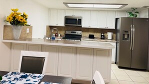 Eine moderne Küche mit weißen Schränken, einem Edelstahl-Kühlschrank, einer Mikrowelle und einer Kaffeemaschine.