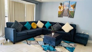 Ein Wohnzimmer mit einem dunkelblauen Ecksofa, einem gemusterten Teppich und Bildern an der Wand.
