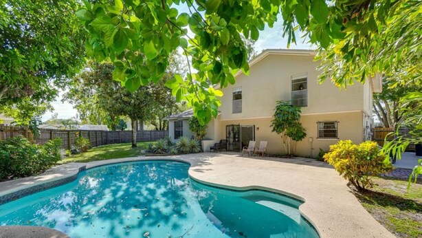 Un patio trasero con piscina, un porche cubierto y una casa.