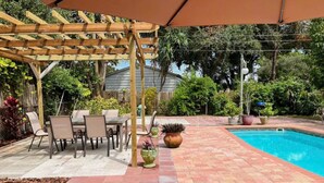 Un patio couvert avec une piscine, des meubles d’extérieur et des plantes en pot.