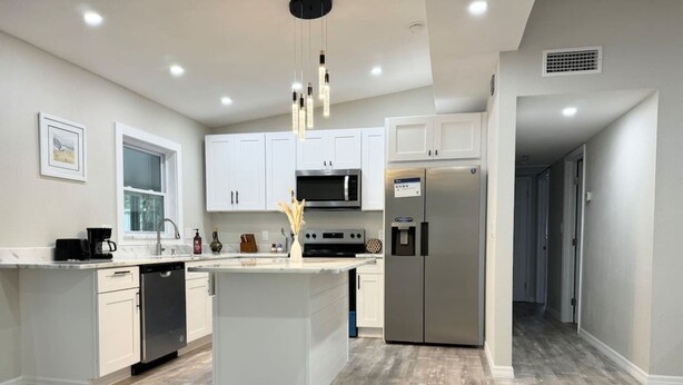 Une cuisine moderne avec des meubles blancs, un îlot central, des appareils en acier inoxydable et un plancher en bois.