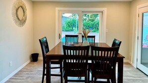 Un coin repas avec une grande table et six chaises, un élément décoratif mural et une vue sur un jardin, visible à travers une porte vitrée.