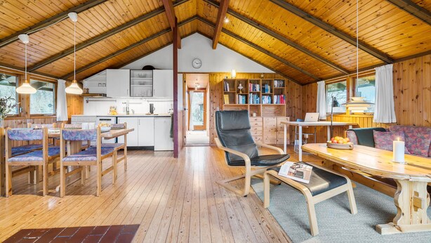 A cozy cabin interior with a wooden ceiling, a dining area with benches, a kitchen with white cabinets, and a bookshelf filled with books. - 3 bedroom beautiful home in Hundested (Hundested)