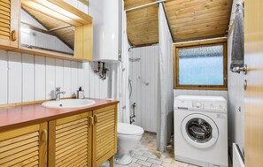 A compact bathroom with a wooden vanity, a sink, a toilet, a shower, and a washing machine. - 3 bedroom beautiful home in Hundested (Hundested)