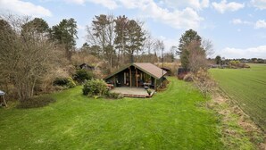 A rustic cabin with a porch, surrounded by a grassy field and trees. - 3 bedroom beautiful home in Hundested (Hundested)