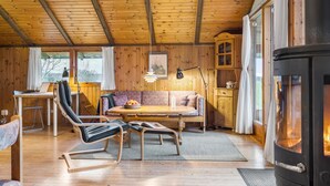 A cozy cabin interior with a wooden ceiling, a sofa, a dining table, a fireplace, and a desk with a chair. - 3 bedroom beautiful home in Hundested (Hundested)