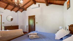 A bedroom with a wooden ceiling, a bed with blue bedding, a mirror, a radiator, and a door.