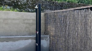 A black vertical structure with a showerhead, a concrete wall, and a bamboo fence.