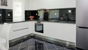 A modern kitchen with white cabinets, a black countertop, and a stainless steel refrigerator. - Villa in Croatia Near Blue & Red Lakes (Imotski)