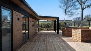 En moderne træterrasse med glasafskærmning, et træspabad og et pergola-konstruktion.
