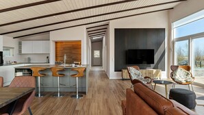 Et moderne køkken med en central ø, barstole og et spisebord. Der er et opholdsområde med en sofa og et fjernsyn.