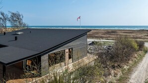 Et moderne hus med mørkt tag, store vinduer og havudsigt.