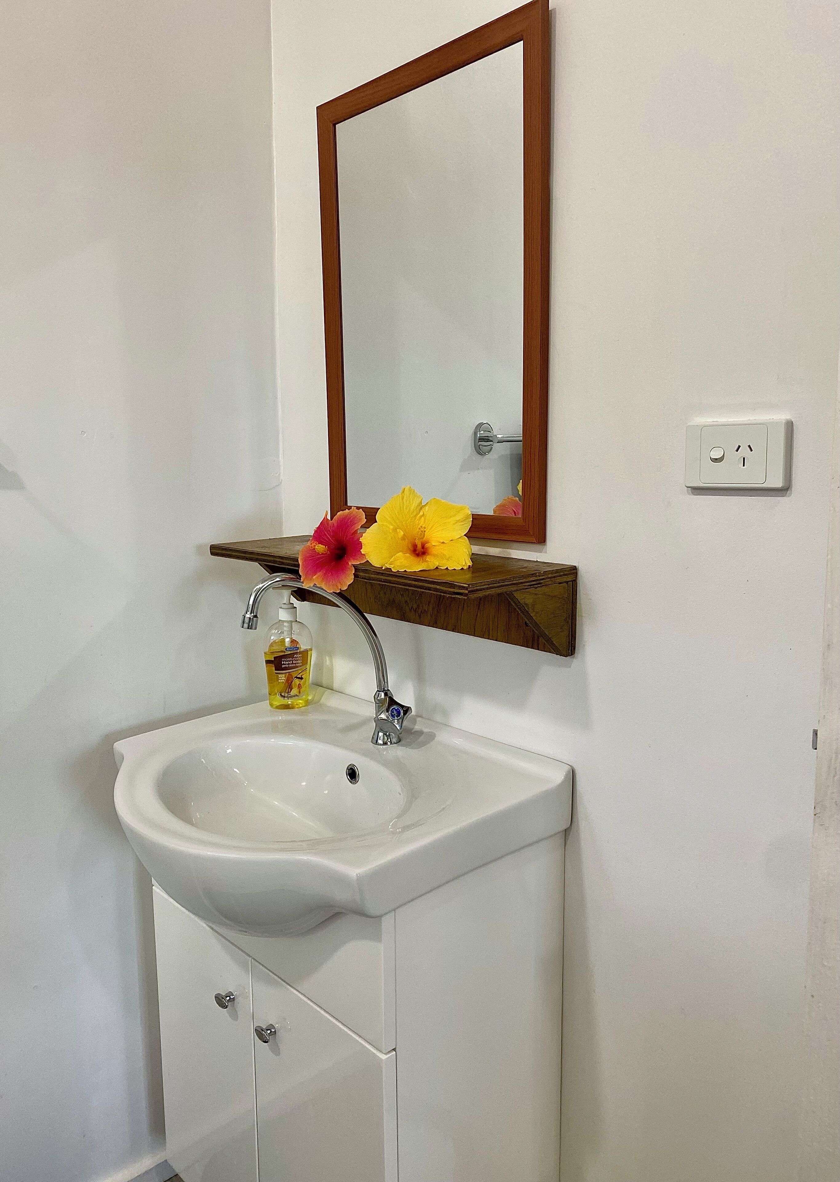 Un baño con un lavamanos blanco, un estante de madera encima y un espejo.