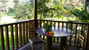 Une terrasse en bois avec une table ronde et deux chaises, entourée d’une végétation luxuriante et d’arbres.