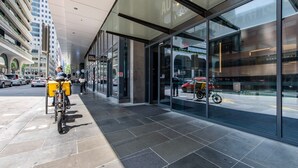 A modern building with large glass windows, a covered entrance, and a bicycle parked outside. - Relax & Recharge 1-Bedroom Apartment with Pool and Gym (Melbourne)