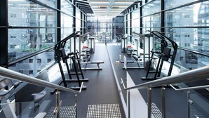 A modern gym with treadmills, weight machines, and a staircase leading to an upper level. - Relax & Recharge 1-Bedroom Apartment with Pool and Gym (Melbourne)