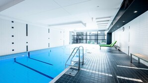 An indoor swimming pool with clear blue water, tiled walls, and a modern design. - Relax & Recharge 1-Bedroom Apartment with Pool and Gym (Melbourne)