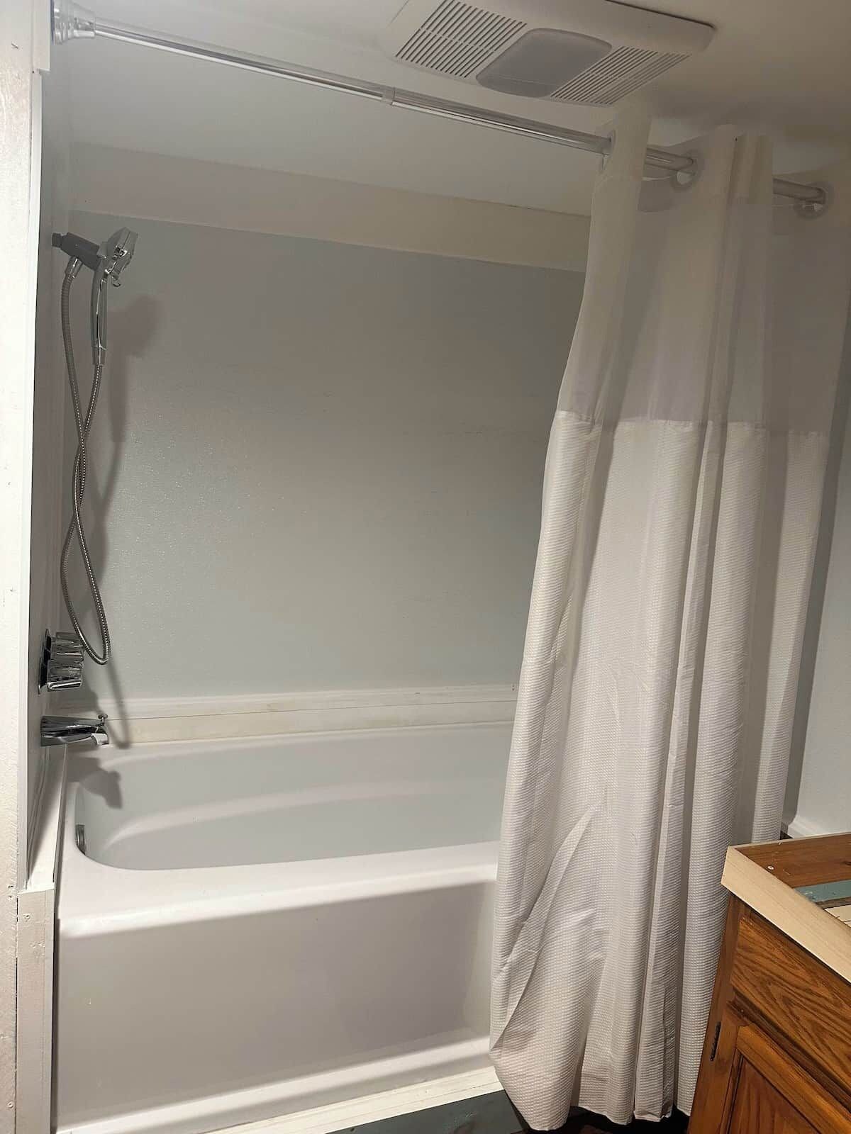 A bathroom with a bathtub, shower, and a wooden vanity.
