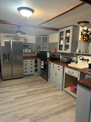 A modern kitchen with a stainless steel refrigerator, built-in oven, and microwave. There are cabinets with glass doors, a wooden countertop, and a ceiling light fixture.