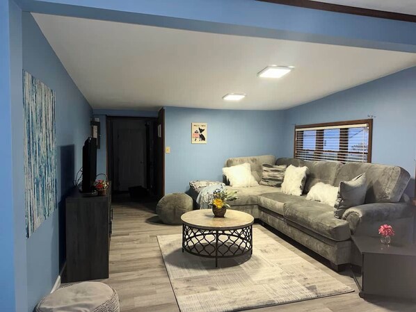 A living room with a sectional sofa, a round coffee table, and a television on a stand.