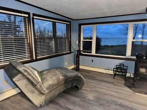 A room with a curved gray sofa, a fireplace, and large windows overlooking a body of water. - Spacious 4-bedroom house in charming Ransomville with WiFi (Ransomville)