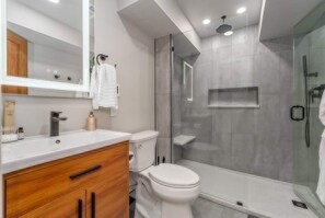 A modern bathroom with a glass shower enclosure, a white sink, and a wooden vanity. - Astoria on Yellowstone (Sioux Falls)