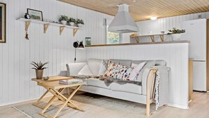 A cozy living room with a sofa, a small wooden table, and a kitchen area with a white refrigerator. - 3 bedroom awesome home in Ringkøbing (Ringkøbing)