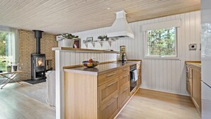A modern kitchen with a wood stove, wooden cabinets, and a large window. - 3 bedroom awesome home in Ringkøbing (Ringkøbing)