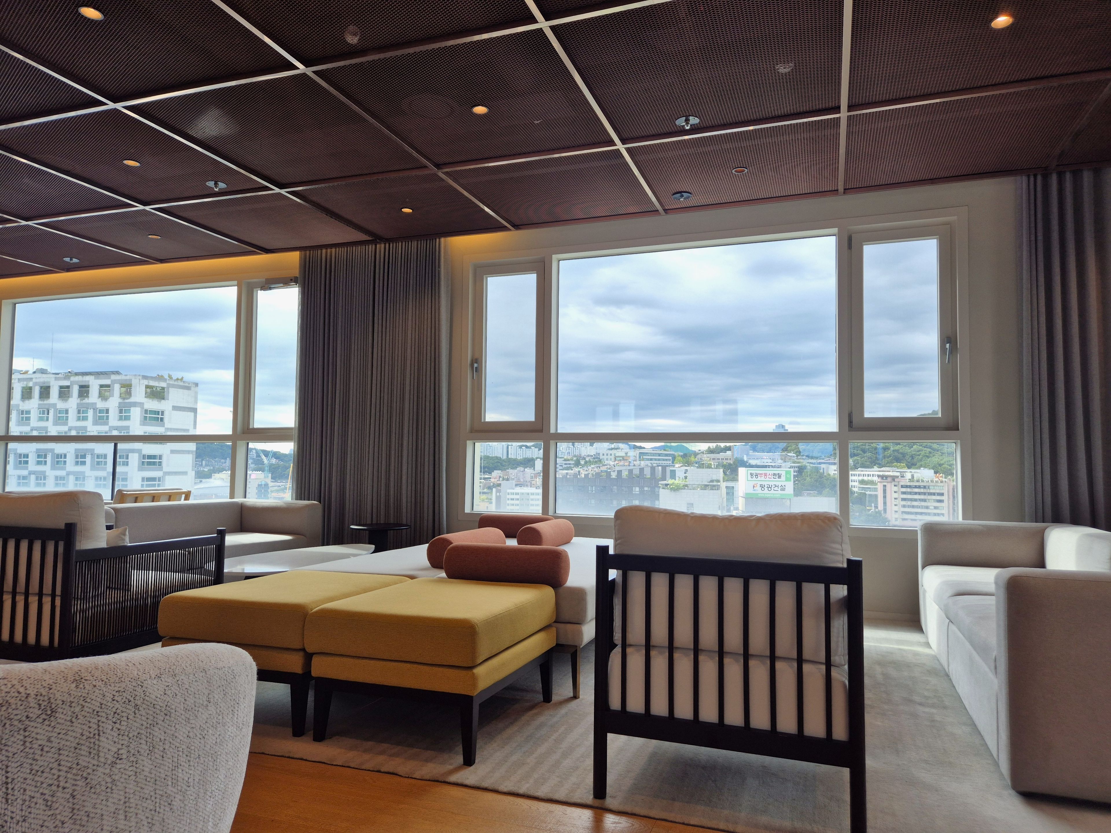 A modern hotel room with a large window, a sofa set, and a wooden ceiling.