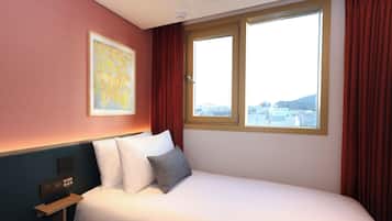 Ein Hotelzimmer mit Bett, Nachttisch, einem Gemälde und einem Fenster mit Vorhängen.