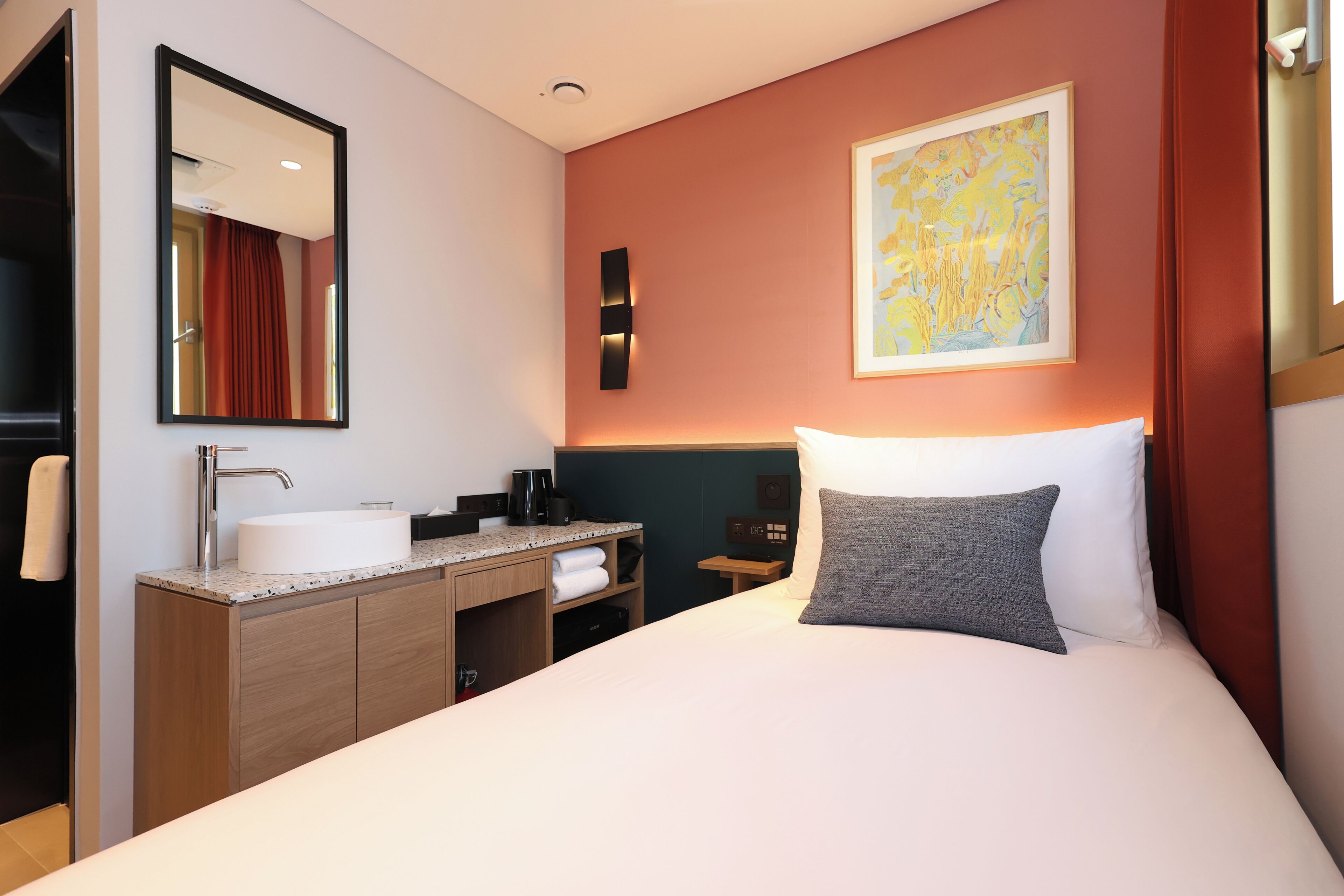 Une chambre d’hôtel avec un lit, un meuble-lavabo, un miroir et un tableau au mur.