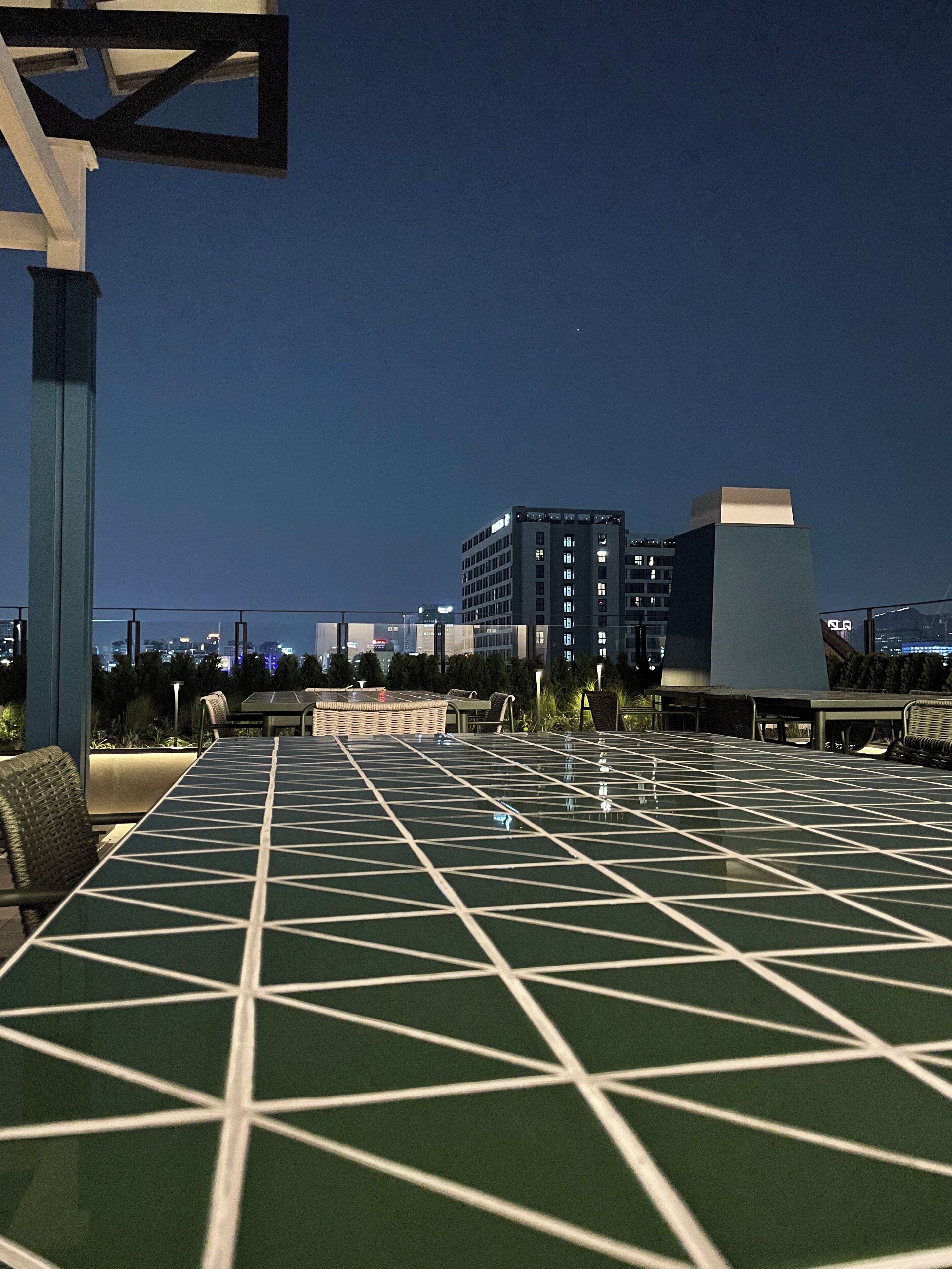 An outdoor seating area with a geometric patterned table, chairs, and a view of a cityscape at night.