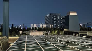 An outdoor seating area with a geometric patterned table, chairs, and a view of a cityscape at night.