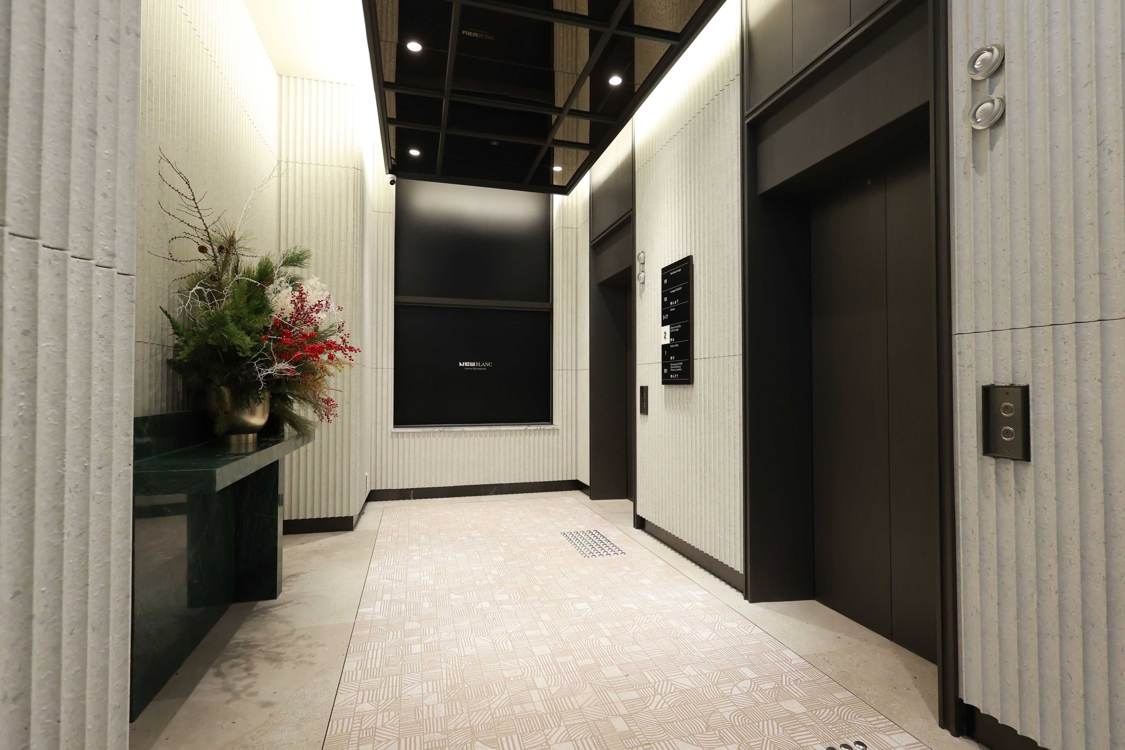 A modern hallway with a patterned floor, a reception desk with a vase of flowers, and an elevator.