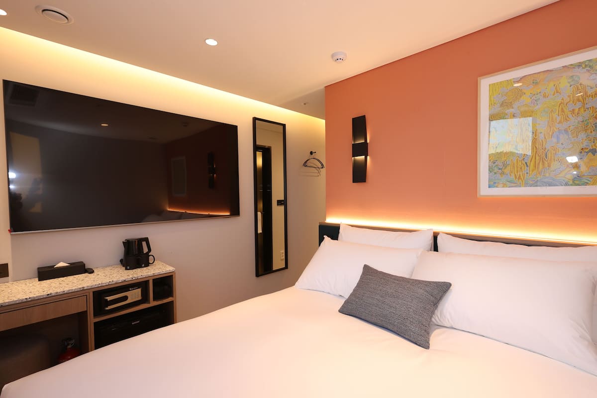 A hotel room with a large bed, a flat-screen TV, a coffee maker, a desk with a computer, and a framed artwork on the wall.