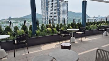 Eine Dachterrasse mit Außenbestuhlung und Blick auf eine Stadtansicht, mit einem Gebäude im Hintergrund.