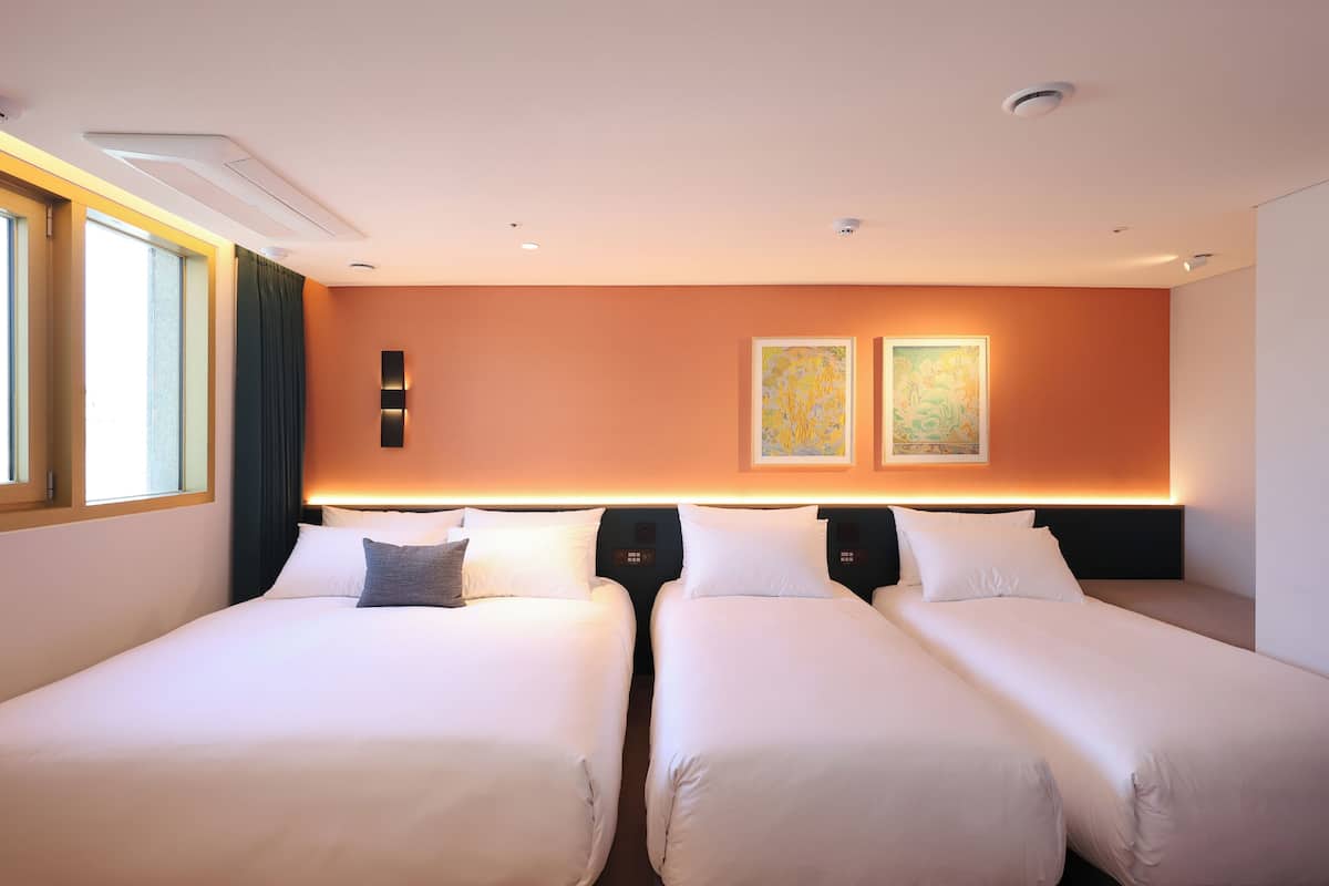 A hotel room with two beds, a large window, and artwork on the wall.