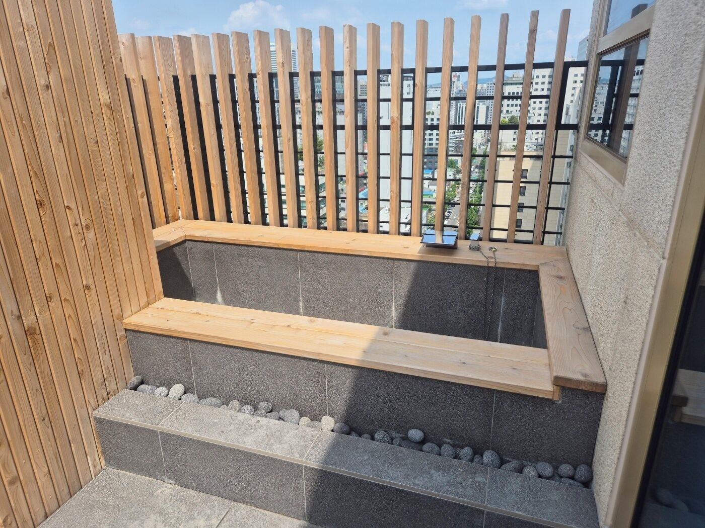A small outdoor seating area with a wooden bench and stone steps, surrounded by a wooden fence.
