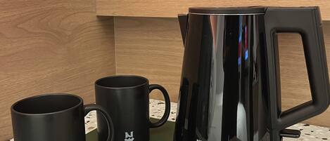 A kitchenette with a black coffee maker, two black mugs, a green tray, and two packets of tea.