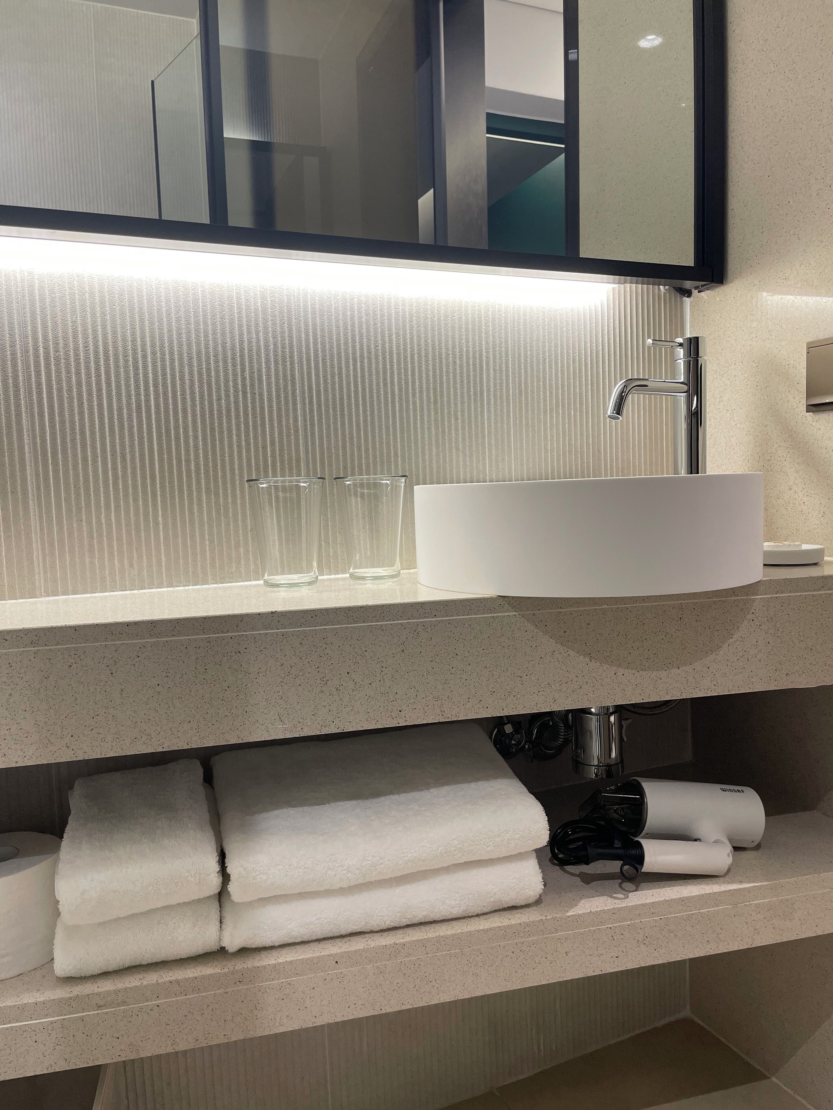 A modern bathroom with a large mirror, a white sink, and a towel rack.