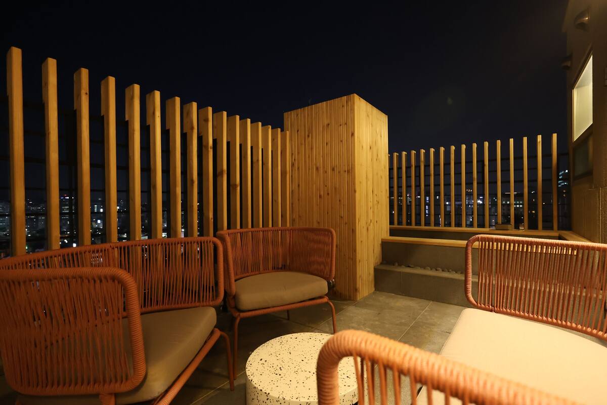A rooftop terrace with wicker furniture and a city view at night.