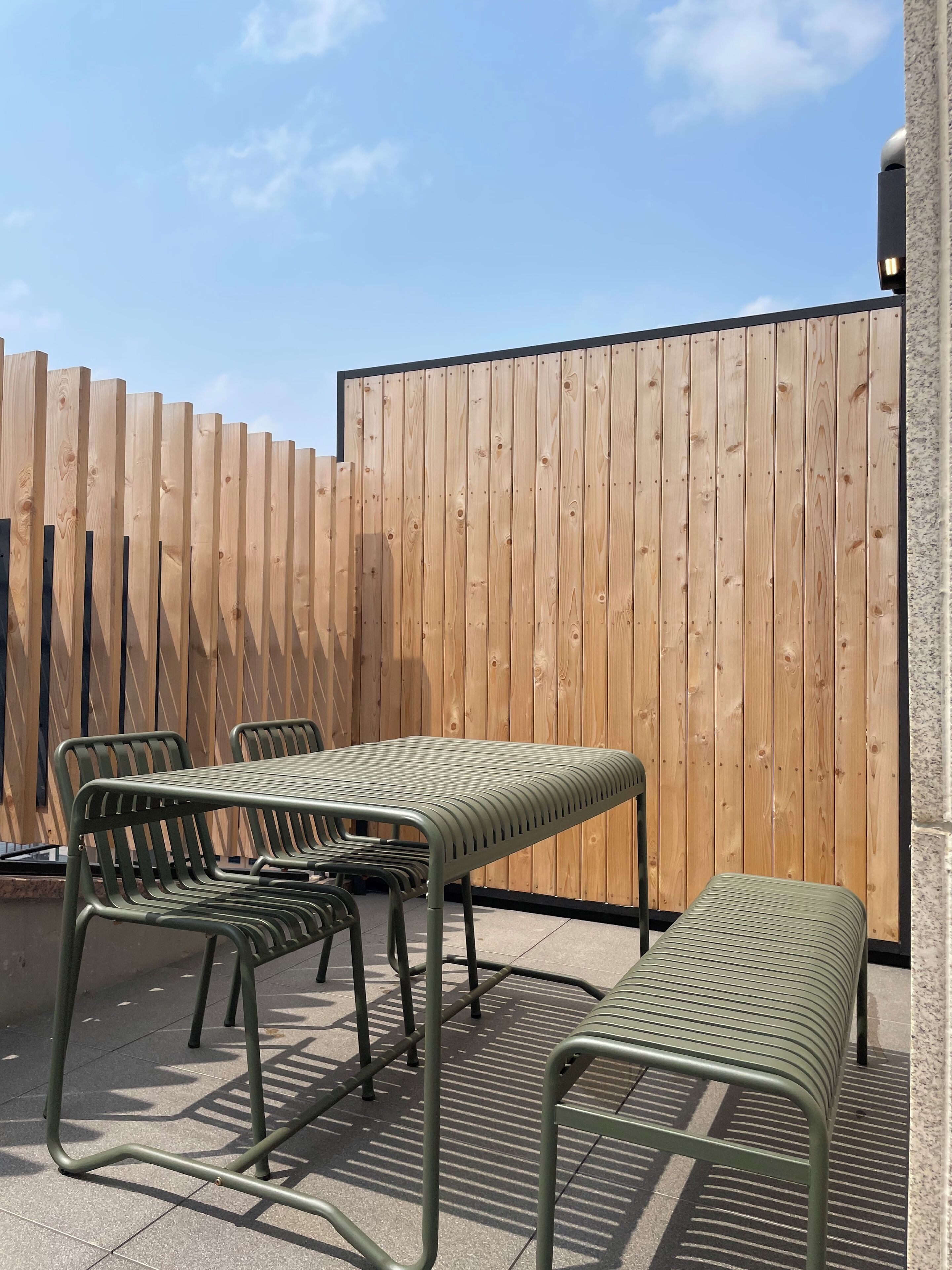 A patio area with a wooden fence, a metal table, and metal chairs.