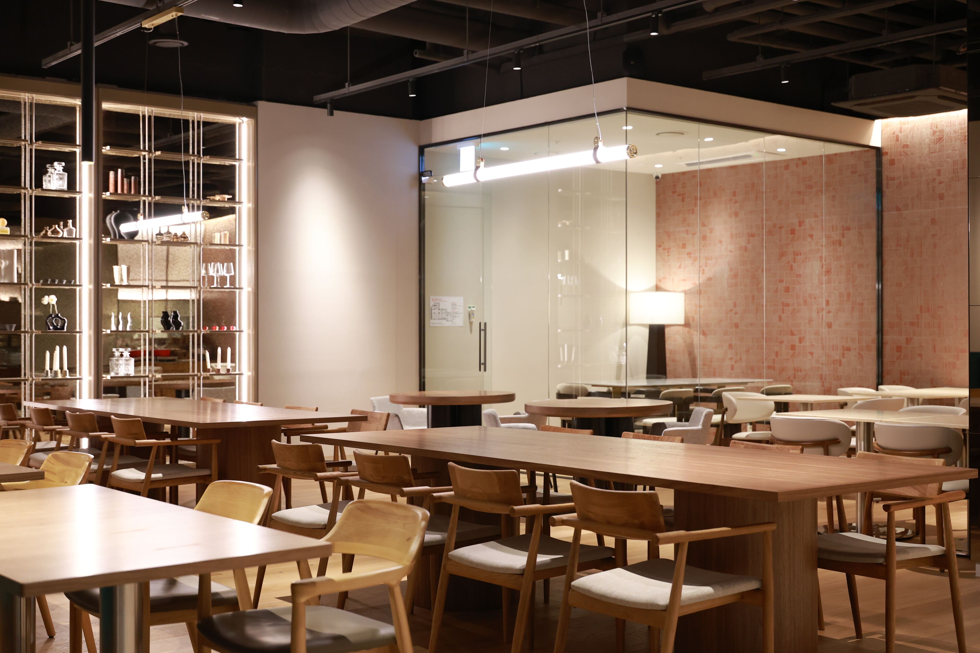 Un moderno comedor con varias mesas y sillas, un panel de vidrio y una pared con diseño decorativo.